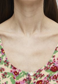 Tejido con estampado floral sobre una base crema, con flores rosas y rojas. Escote en forma de barco con un detalle de botón blanco en la parte delantera.