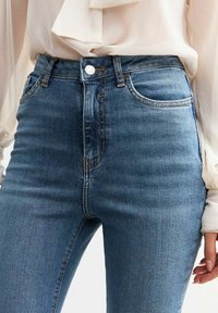 Hoge taille blauwe denim jeans met een slim fit, voorzien van zijzakken, een knoopsluiting en zichtbare stikseldetails.