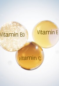 Trois capsules sphériques avec des contenus étiquetés : Vitamine B3 (or scintillant), Vitamine E (jaune transparent) et Vitamine C (ambre).