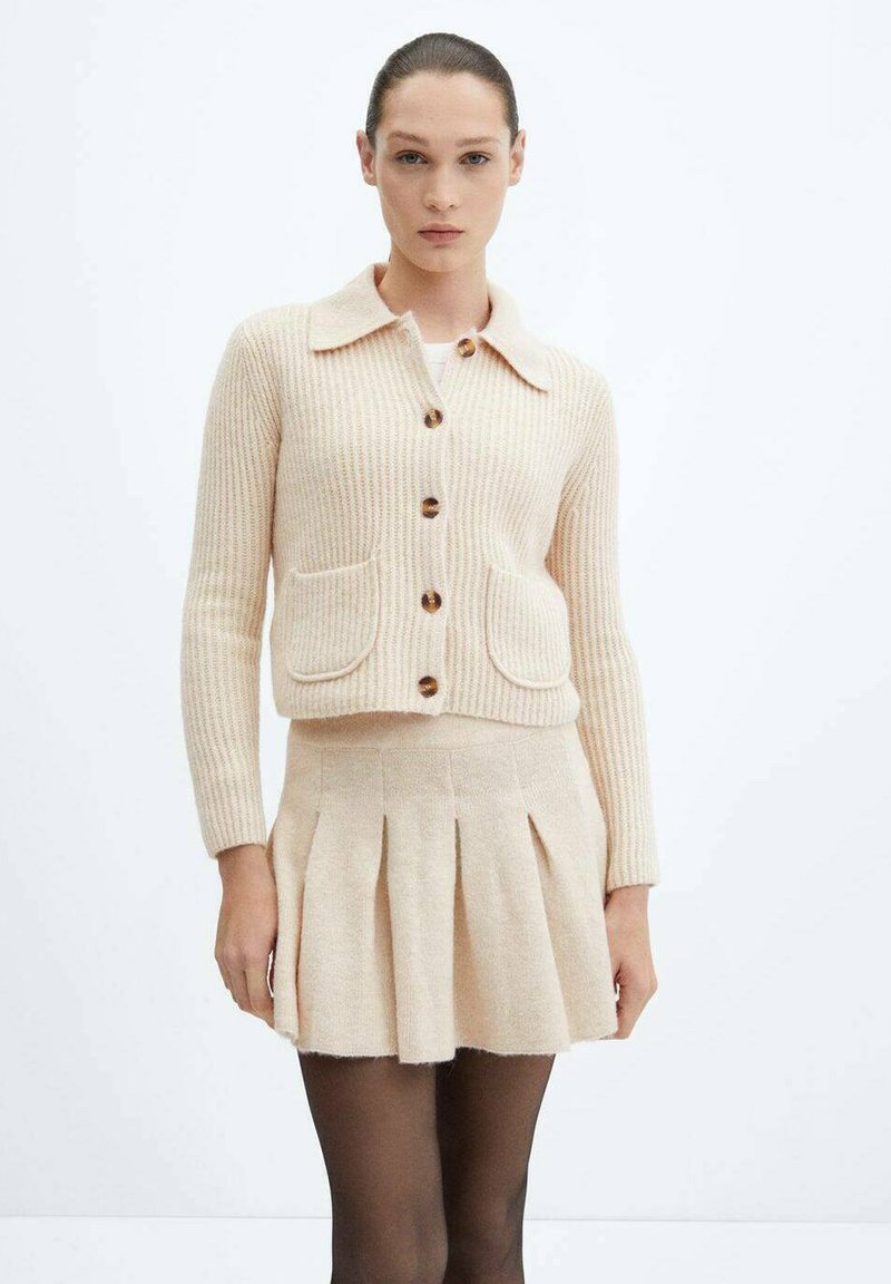 Cardigan a coste beige pallido con colletto e chiusura a bottoni, abbinato a una gonna plissettata coordinata, entrambi realizzati in morbido materiale jersey.