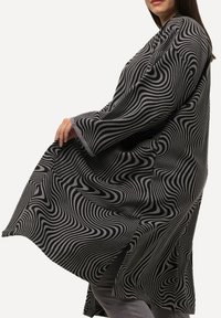 Langes, locker sitzendes Kleidungsstück mit einem gewellten Muster in Schwarz und Grau, das breite Ärmel und seitliche Schlitze für mehr Bewegungsfreiheit aufweist.
