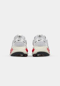 Vue arrière de baskets blanches Nike avec une tige texturée, des accents rouges et une semelle en caoutchouc noir présentant un motif de semelle.