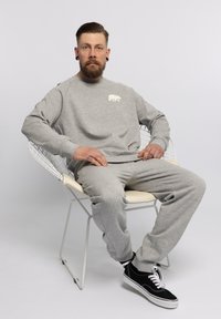 Grijze fleece sweatshirt met een witte berenafbeelding op de borst, gecombineerd met bijpassende grijze sweatpants en zwarte sneakers.