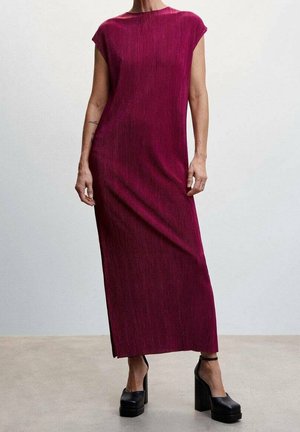 Femme portant une robe maxi sans manches côtelée, de couleur magenta foncé, fendue sur le côté, associée à des chaussures à plateforme à talons hauts noires sur un sol en béton.