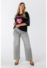 Zwart oversized t-shirt met paillettenaccenten op de mouwen, roze grafische print, gecombineerd met grijze wijde jeans en leopardenprint hakken.