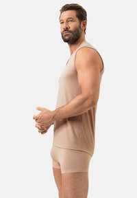 Débardeur beige et boxer assortis en tissu texturé. Design sans manches avec encolure en V, style ajusté, coutures minimales et motifs subtils.