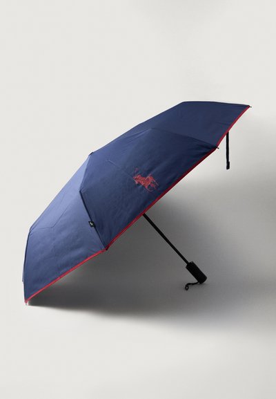 Guarda-chuva azul-marinho com um acabamento em vermelho, apresentando um detalhe de logotipo. Confeccionado em tecido, com um cabo de metal preto e mecanismo de abertura automática.
