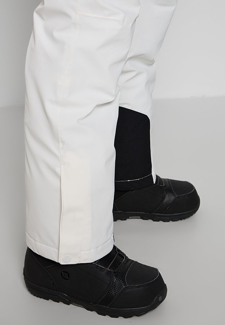 Pantaloni impermeabili bianchi con taglio dritto, abbinati a stivali neri isolati con una finitura testurizzata e chiusura in Velcro.