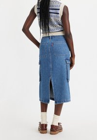 Džínová midi sukně s vysokým pasem, zadním rozparkem, bočními cargo kapsami a dvěma zadními našitými kapsami. Barva: středně modrá.