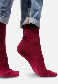 Bordowe skarpetki prążkowane wykonane z miękkiego materiału, z wąskim noskiem i wzmocnionym piętem, noszone z dżinsami z podwiniętymi nogawkami, pokazującymi jasnoniebieskie nitki.