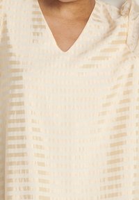 Helle Cremebluse mit V-Ausschnitt, die vertikale, strukturierte Streifen in unterschiedlichen Breiten aufweist und aus einem weichen, glatten Stoff gefertigt ist. Zu den Details gehören gepuffte Ärmel.