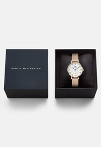 Reloj de oro rosa con correa de malla, cara blanca redonda con números romanos, presentado en una caja negra con letras doradas.