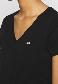 Černé tričko s krátkým rukávem a výstřihem do V, vyrobené z měkkého materiálu, s malým barevným logem na hrudi.