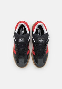 Fekete és piros sportcipők velúr és bőr anyagból, gumi talppal, kerek fűzőkkel és Adidas logóval a nyelvén.