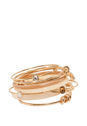 Pile de bracelets jonc dorés et crème, présentant des bandes lisses et des accents de pierres précieuses sur fond blanc.
