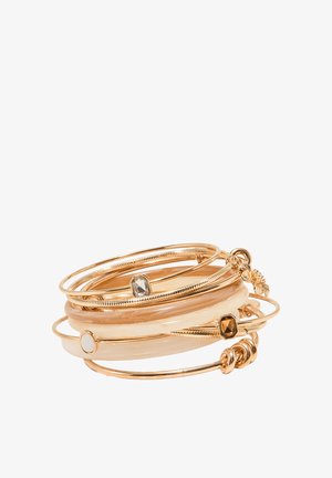 Pile de bracelets jonc dorés et crème, présentant des bandes lisses et des accents de pierres précieuses sur fond blanc.