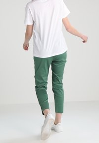 T-shirt blanc en coton et pantalon vert fuselé. Le pantalon présente une texture lisse, une taille élastique et des chevilles retroussées, associé à des baskets blanches.