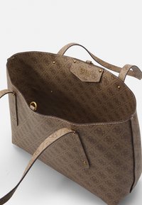 Hnědá taška přes rameno s vzorovaným designem a texturovaným povrchem, se zlatými kovy. Interiér obsahuje označenou etiketu a dvě horní ucha pro nošení.