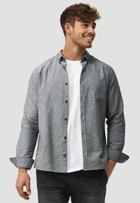 Gray button-up shirt made of textured fabric, featuring a chest pocket, button closure, and rolled cuffs, layered over a white t-shirt.