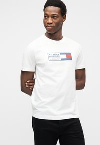 Λευκό βαμβακερό μπλουζάκι με ορθογώνιο γραφικό σε μπλε, κόκκινο και ναυτικό μπλε με το κείμενο "TOMMY HILFIGER". Με κοντά μανίκια και κλασική στρογγυλή λαιμόκοψη.