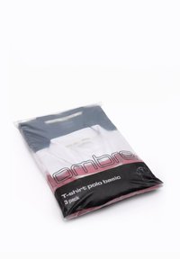 Trepack med grundläggande polo t-shirts i en genomskinlig plastpåse. Innehåller en blandning av färger inklusive vit, marinblå och röda accenter med etikettinformation.