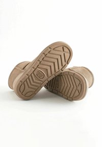 Bottines en suède tan avec semelles en caoutchouc présentant un motif de bande de roulement en zigzag et un logo en relief. Le design est simple et fonctionnel.