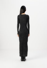 Lång svart ribbad stickad klänning med en figurnära silhuett, långa ärmar och båthals, med subtila texturdetaljer och golvlång fåll.