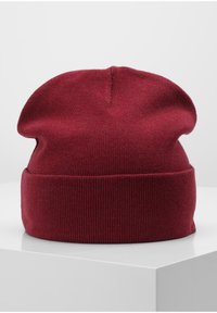 Red knitted beanie with a loose fit, featuring a ribbed cuff. The fabric appears soft and elastic, creating a relaxed shape at the top.