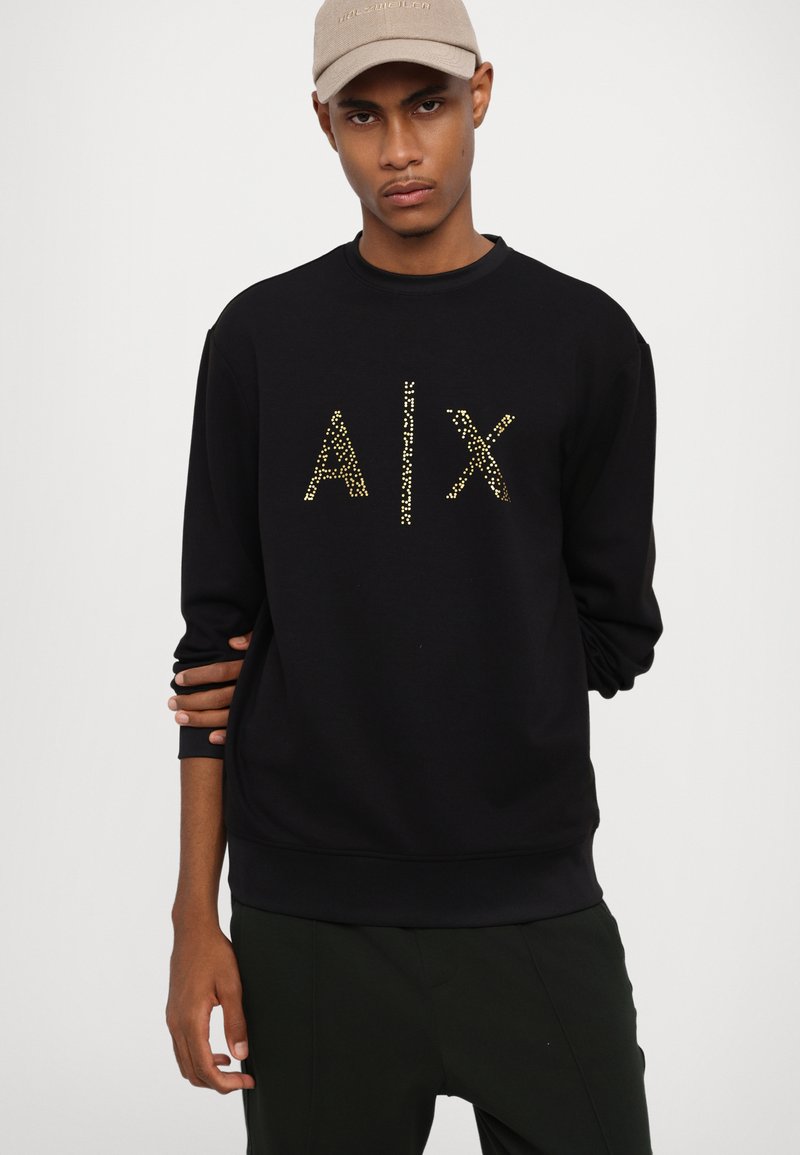 Schwarzer Sweatshirt mit Rundhalsausschnitt und langen Ärmeln, mit goldenen Nietenlettern "AIX" auf der Vorderseite. Glatte Stofftextur.