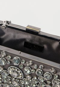 Czarna torebka kopertówka ozdobiona przezroczystymi kryształami, metalową ramką i zapięciem. Posiada gładkie satynowe wnętrze oraz wytłoczoną tabliczkę z logo.