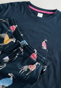 Set de loungewear bleu marin format dintr-o cămașă și pantaloni, decorat cu greyhoundi jucăuși în pulovere colorate și o etichetă de gât cu marcă.