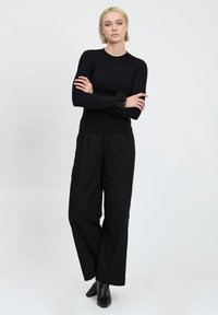 Maglietta nera a maniche lunghe con polsini in pizzo testurizzato, abbinata a pantaloni neri a vita alta con gamba larga e stivaletti neri con punta.