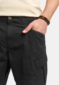 Pantalons cargo noir en tissu léger avec fermeture à bouton, poches latérales et coupe décontractée. Texture subtile visible.