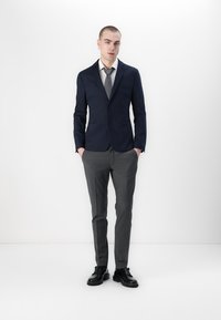 Navy blazer with two buttons, gray dress shirt, and matching gray trousers. Black dress shoes complete the formal outfit. Smooth fabric texture.