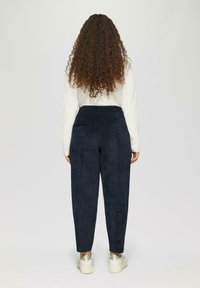 Marineblauwe fluwelen joggers met een ontspannen pasvorm, elastische tailleband en twee achterzakken. Met een gladde textuur en taps toelopende benen.