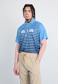 Light blue polo shirt with navy stripes and white "AIR" logo; paired with beige pants, featuring an elastic waistband and side pockets.