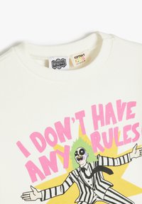 Sweatshirt en coton blanc avec une impression graphique d'un personnage aux cheveux verts et en costume rayé. Le texte indique : "JE N'AI AUCUNE RÈGLE."