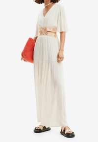 Bílé, splývavé maxi šaty s V-výstřihem a krátkými rukávy; zdobené vyšívaným páskem v žluté a modré barvě. Doplněné korálovou psaníčkem.