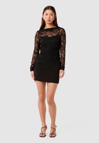 Μαύρη δαντελένια μπλούζα με μακριά μανίκια, συνδυασμένη με ένα εφαρμοστό μαύρο μίνι φόρεμα. Περιλαμβάνει μια υφασματένια κορυφή και λείες φούστα. Στυλιζαρισμένο με μαύρες σανδάλια με λουριά.