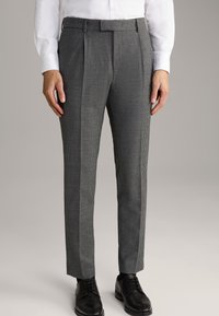 Strukturierte Schwarz-Weiß-Karohosen mit tailliertem Schnitt, die zwei vordere Falten aufweisen und mit schwarzen Schnürschuhen kombiniert sind.