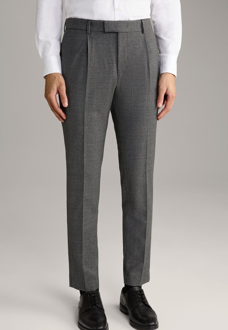 Strukturierte Schwarz-Weiß-Karohosen mit tailliertem Schnitt, die zwei vordere Falten aufweisen und mit schwarzen Schnürschuhen kombiniert sind.