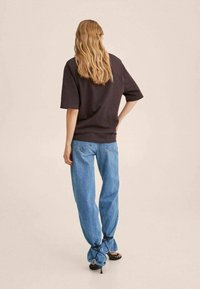 Mørkebrun oversized t-shirt kombineret med lyseblå lige ben jeans, med snoretræk detaljer ved ærmerne og snørrede sandaler.