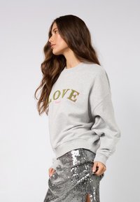 Szürke pulóver, melyen a "LOVE" szó élénk zöld és rózsaszín hímzéssel van díszítve. Ezüst flitteres szoknyával párosítva.