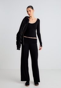 Μαύρο τοπ με μακριά μανίκια, λαιμόκοψη scoop, σετ με μαύρο παντελόνι φαρδιάς γραμμής. Το μοντέλο κρατάει επίσης ένα μαύρο σακάκι. Λείο υλικό, μινιμαλιστικός σχεδιασμός.