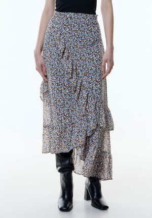 Floral maxi Rock mit einem voluminösen Saum in hellblau, orange und weißen Mustern. Leichter Stoff mit fließendem Design. Kombiniert mit schwarzen kniehohen Stiefeln.