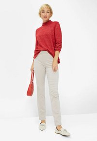 Rød strikket turtleneck sweater, lys beige slim-fit bukser, hvide flade sko med sløjfedetalje og en lille rød håndtaske. Enkel, afslappet outfit.
