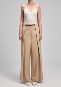 Pantalons beige à jambe large avec plis, associés à un body blanc à côtes. Les pantalons sont dotés d'une ceinture noire. Texture lisse, design minimaliste.