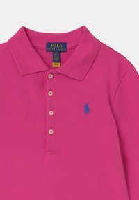 Vaaleanpunainen puuvillapolo-paita, jossa on tekstuurinen pinta. Varustettu sinisellä brodeeratulla logolla ja kolmella napilla kauluksessa.