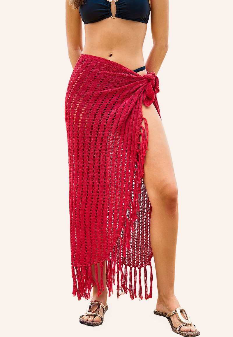 Rode gebreide strandsarong met een open weefsel, franjes onderaan en een samengebonden knoop aan de zijkant, gedragen over een zwart bikini.