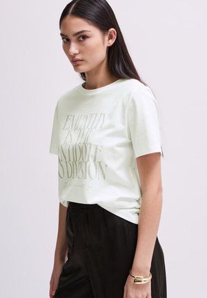 T-shirt vert clair à manches courtes avec un grand graphique de texte dans une teinte plus foncée. Tissu doux, coupe décontractée, associé à un pantalon sombre.